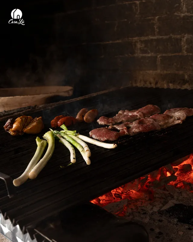 Cortes de carne y cebollines asándose sobre la parrilla de Casa Lú